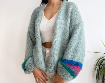 May include: A light blue fuzzy cardigan with colorful stripes on the cuffs. The cardigan is open and has a V-neck.