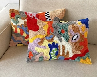 May include: Two colorful abstract patterned throw pillows with a variety of colors including red, orange, yellow, green, blue, and purple. The pillows are on a light beige couch.