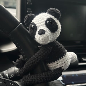 以下が含まれることがあります： 黒と白の毛糸で編まれたパンダのぬいぐるみが車のハンドルにぶら下がっている