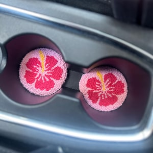 May include: Two pink and red car cup holders with a hibiscus flower design.