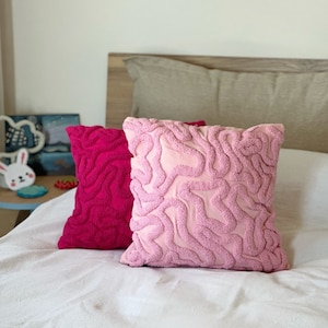 May include: Two decorative throw pillows with a textured, wavy pattern. The pillow on the left is pink and the pillow on the right is a darker shade of pink.