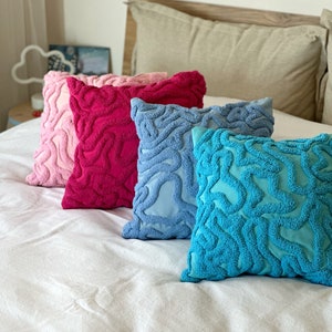 May include: Four decorative throw pillows with a textured, wavy pattern. The pillows are in shades of pink, red, blue, and turquoise.