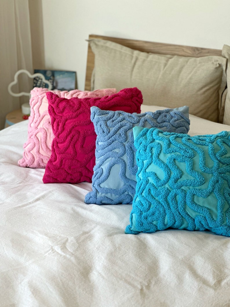 May include: Four decorative throw pillows with a textured, wavy pattern. The pillows are in shades of pink, red, blue, and turquoise.