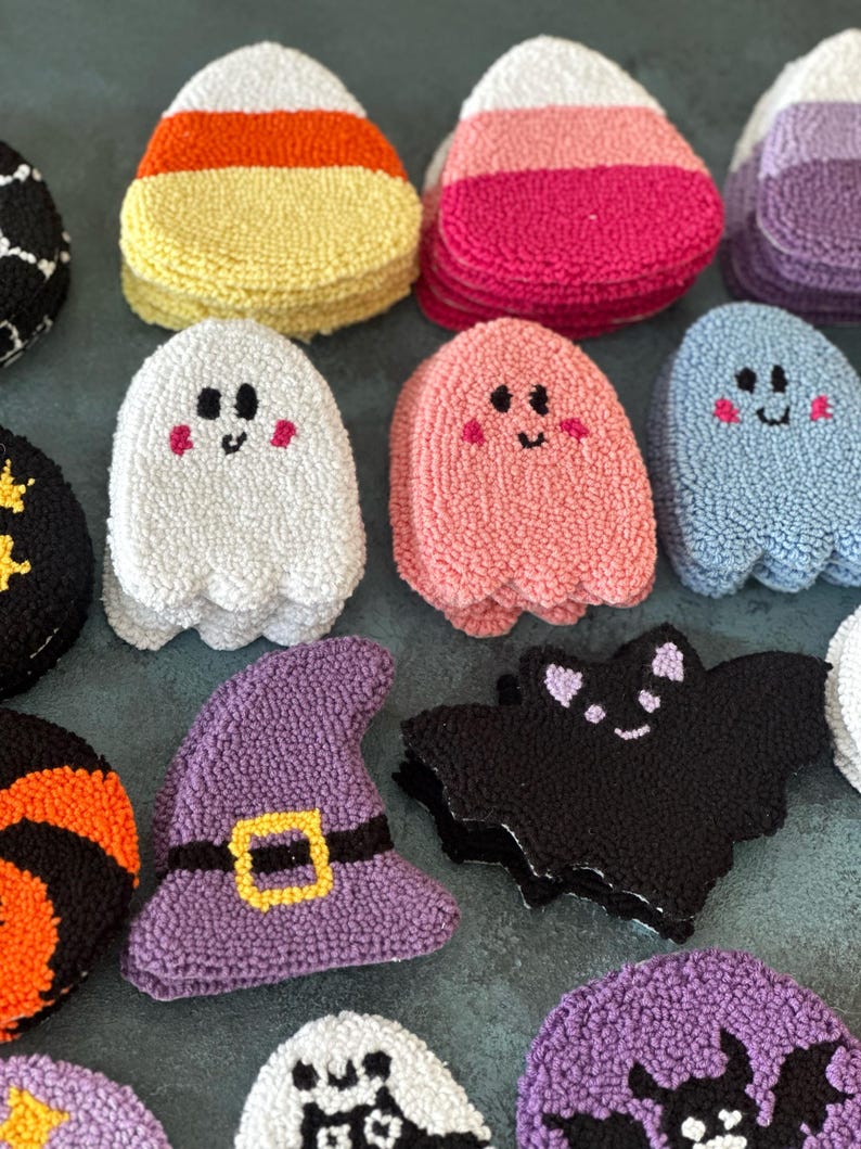 May include: A collection of colorful, textured Halloween-themed decorations. The assortment includes candy corn, ghosts, a witch's hat, and bats. The decorations are made of a soft, looped material and feature embroidered details.