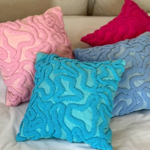 May include: Four decorative throw pillows with a unique, textured, abstract design. The pillows are in shades of pink, blue, turquoise, and magenta.