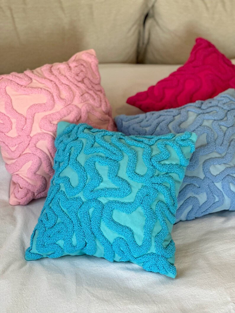 May include: Four decorative throw pillows with a unique, textured, abstract design. The pillows are in shades of pink, blue, turquoise, and magenta.