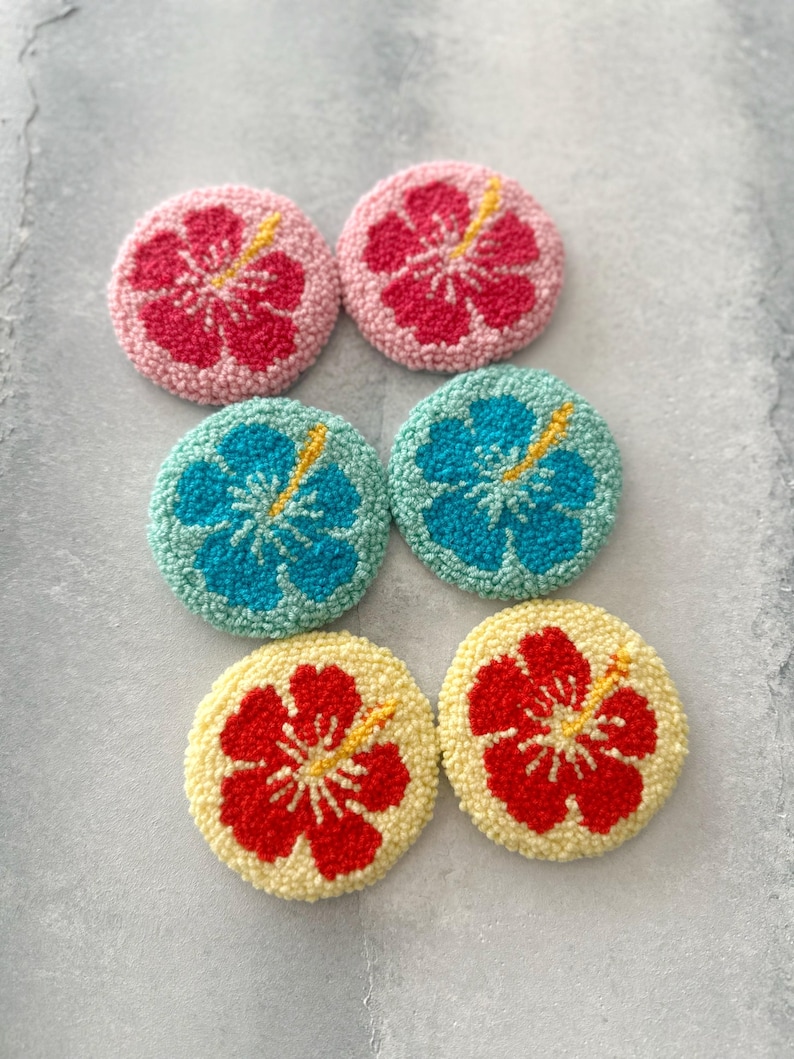 May include: Six round, colorful, felt flower coasters with a hibiscus design. The coasters are in pink, blue, red, and yellow.