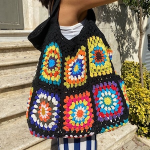 May include: A black crochet tote bag with colorful granny square designs. The bag has a wide, open top and two long straps.
