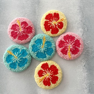 May include: Six colorful round felt coasters with a yellow hibiscus flower design. The coasters are in shades of pink, red, yellow, blue, and green.