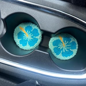 May include: Two blue and green car cup holders with a yellow hibiscus flower design.