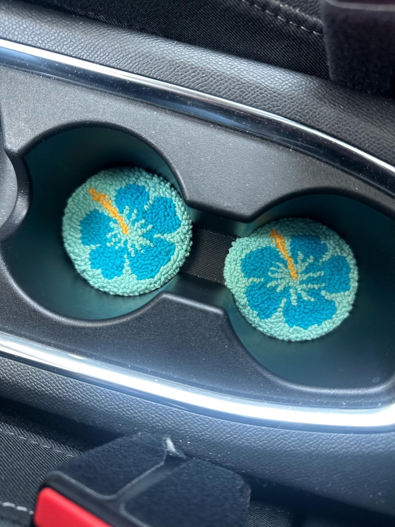 May include: Two blue and green car cup holders with a yellow hibiscus flower design.