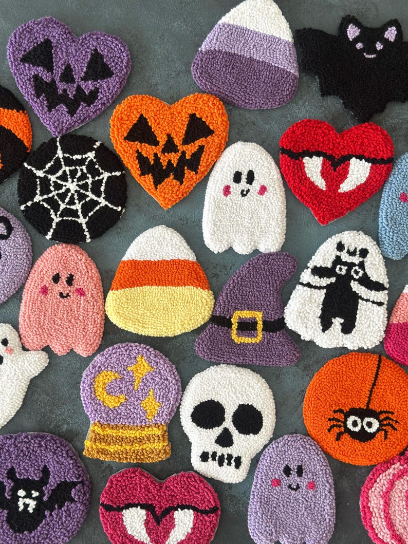 May include: A collection of colorful, textured Halloween-themed coasters. Designs include jack-o'-lanterns, ghosts, bats, spiders, candy corn, and a skull. The coasters are in various shapes, including hearts, circles, and a witch's hat.