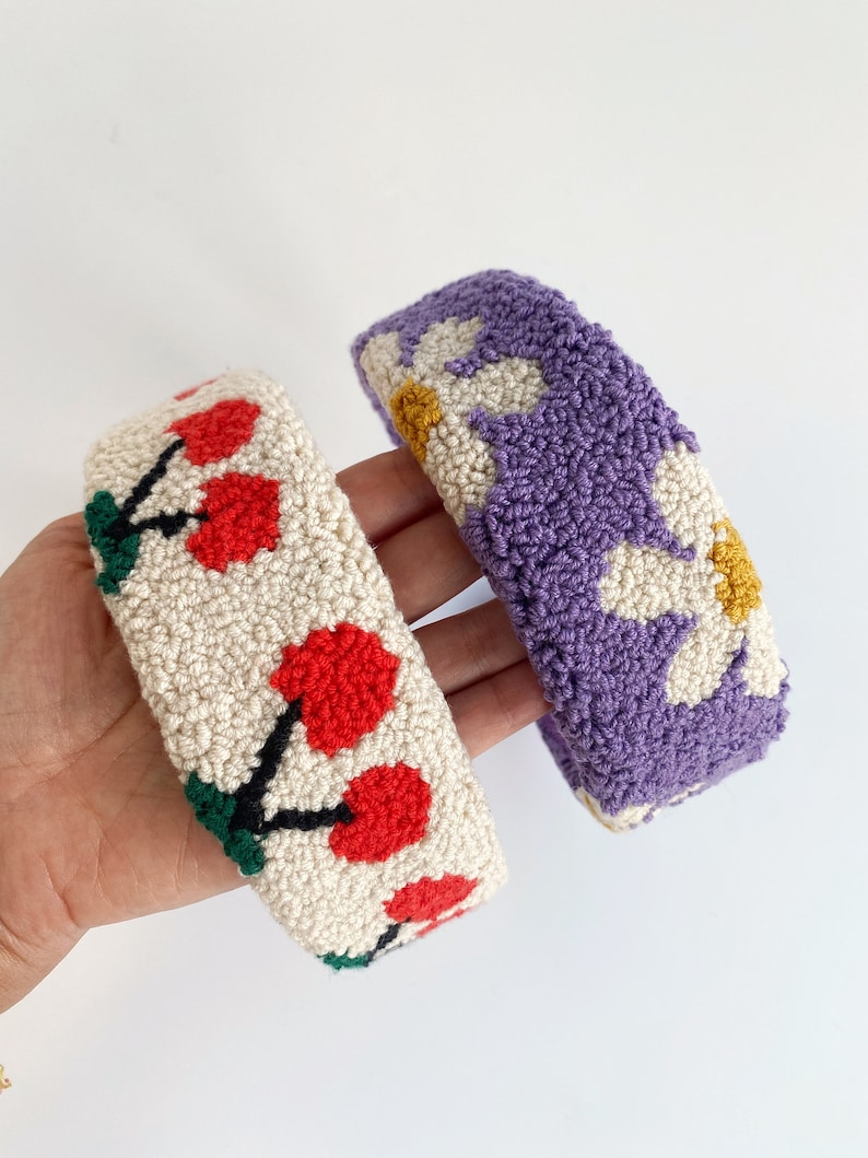 Pu&ograve; includere: Due fasce per capelli fatte a mano, una con sfondo bianco e ciliegie rosse, l'altra con sfondo viola e margherite bianche.