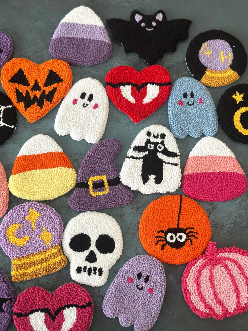 May include: A collection of colorful, handmade Halloween-themed coasters. Designs include a jack-o'-lantern, ghost, bat, spider, skull, witch hat, and candy corn. The coasters are made with a textured, looped yarn technique.