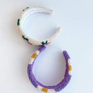 Pu&ograve; includere: Due accessori per capelli a forma di fascia. Uno &egrave; bianco con fiori ricamati rossi e verdi. L'altro &egrave; viola con strisce gialle e bianche.