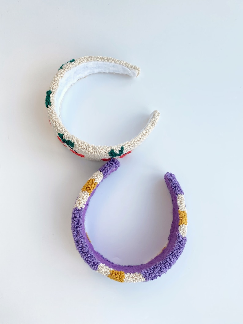 Pu&ograve; includere: Due accessori per capelli a forma di fascia. Uno &egrave; bianco con fiori ricamati rossi e verdi. L'altro &egrave; viola con strisce gialle e bianche.