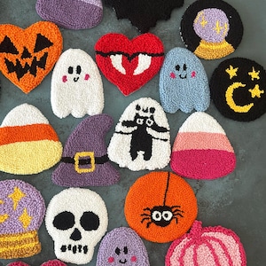 May include: A collection of Halloween-themed, textured coasters in various shapes and colors. Designs include a jack-o'-lantern, ghost, bat, candy corn, witch hat, skull, spider, and pumpkin. The coasters are made of a soft, plush material.
