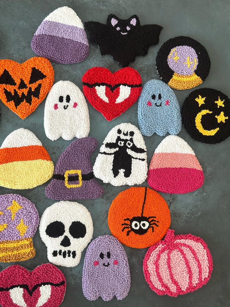 May include: A collection of Halloween-themed, textured coasters in various shapes and colors. Designs include a jack-o'-lantern, ghost, bat, candy corn, witch hat, skull, spider, and pumpkin. The coasters are made of a soft, plush material.