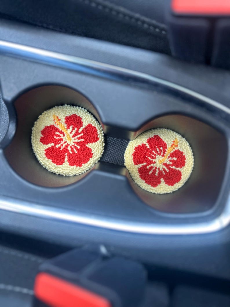 May include: Two red and yellow hibiscus flower-shaped car coasters in a car cup holder.
