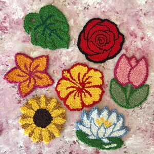 May include: A collection of colorful, handmade floral and leaf-shaped textile art pieces. The designs include a green leaf, a red rose, a yellow sunflower, and other flowers in shades of pink, yellow, and orange.