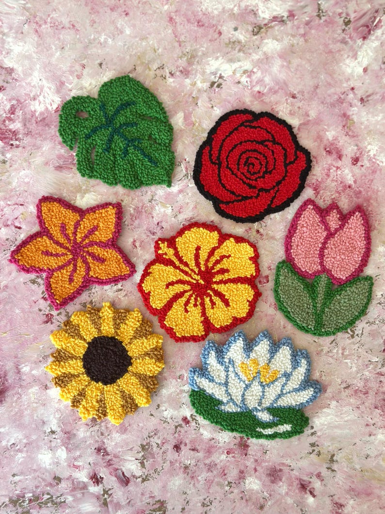 May include: A collection of colorful, handmade floral and leaf-shaped textile art pieces. The designs include a green leaf, a red rose, a yellow sunflower, and other flowers in shades of pink, yellow, and orange.