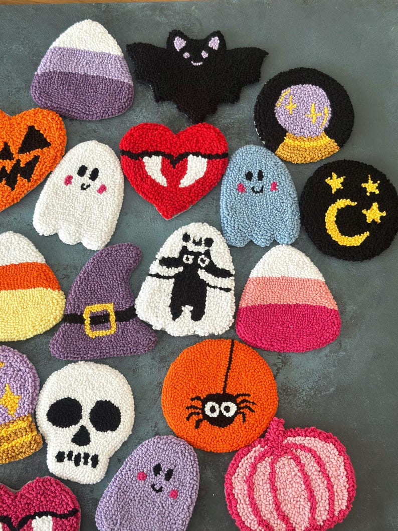 May include: A collection of colorful, textured Halloween-themed coasters. Designs include a bat, ghosts, candy corn, a skull, a witch's hat, a spider, a pumpkin, a heart, and a fortune-telling ball. The coasters are made of a soft, plush material.