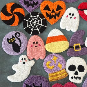 May include: A collection of Halloween-themed, textured, decorative items. Includes a variety of shapes such as pumpkins, ghosts, bats, and skulls, in colors like orange, purple, black, and white. The items appear to be handmade and are arranged on a flat surface.
