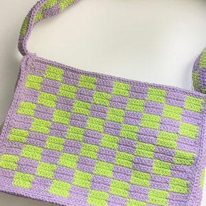 May include: A purple and green checkered crochet shoulder bag. The bag has a long strap and is made of a soft, textured yarn.