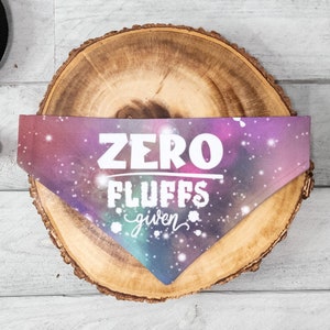 May include: A purple and blue galaxy print dog bandana with white text that reads "ZERO FLUFFS given".