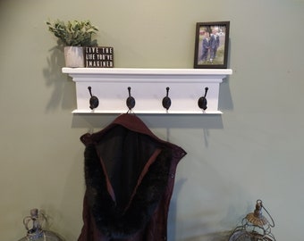 May include: White coat rack with four black hooks and a shelf. The shelf has a small potted plant and a sign that reads "Live the life you've imagined".