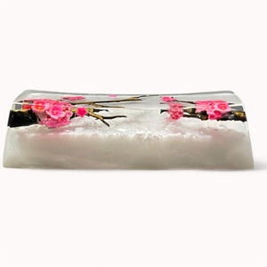 Peut inclure: Un repose-poignets rectangulaire transparent avec une base blanche et des fleurs de cerisier roses incrust&eacute;es &agrave; l'int&eacute;rieur. Les fleurs sont dispos&eacute;es en forme de branche.