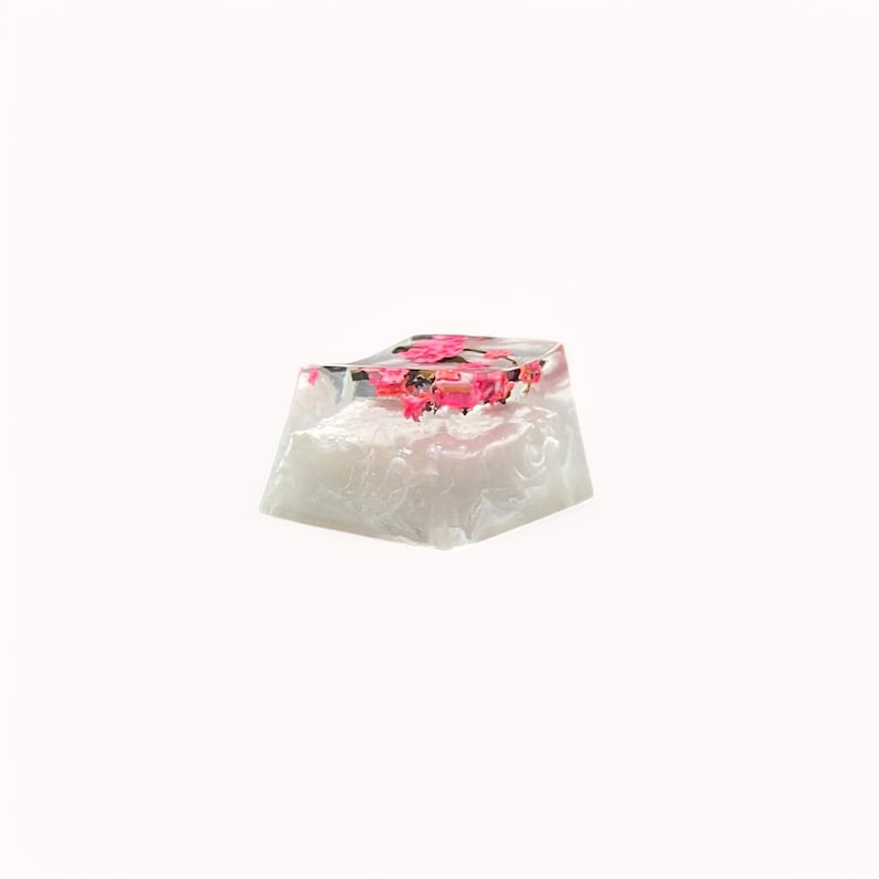 Peut inclure: Un capuchon de touche en r&eacute;sine transparente avec des fleurs roses incrust&eacute;es &agrave; l'int&eacute;rieur. Le capuchon de touche est blanc et a une surface textur&eacute;e.