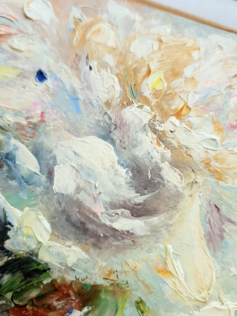 May include: Close-up of an oil painting featuring a textured floral arrangement. The artwork showcases thick brushstrokes in shades of white, cream, and light brown, with hints of blue, pink, and green. The painting is framed.