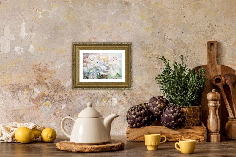 May include: A still life featuring a framed painting with a gold frame, a white teapot, lemons, artichokes, and rosemary. The painting has a floral theme. The scene is set on a wooden surface.