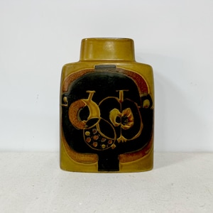 May include: A rectangular, mustard-colored ceramic vase with a dark brown and black apple design. The vase has a cylindrical neck and a decorative pattern of apples and leaves.