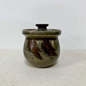 May include: A small, brown and gray ceramic jar with a lid. The jar has a swirl pattern and is decorated with brown and red accents.
