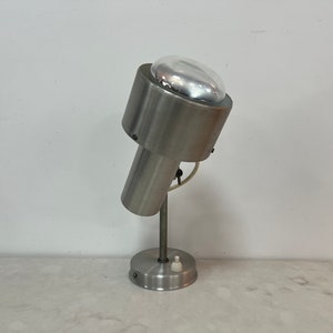 May include: A silver metal desk lamp with a round, white, frosted glass shade. The lamp has a simple, modern design and a single switch on the base.
