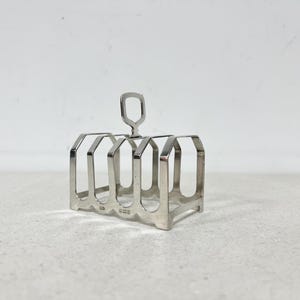 May include: A silver-colored toast rack with six slots and a handle. The rack has a rectangular shape with a handle at the top. The design is simple and functional, suitable for serving toast at the breakfast table.