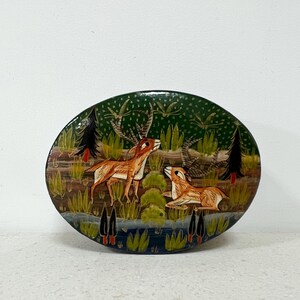 May include: Oval decorative plate with a hand-painted forest scene. Two deer are depicted in a forest with tall grass, trees, and a body of water. The plate has a dark green background with a glossy finish.
