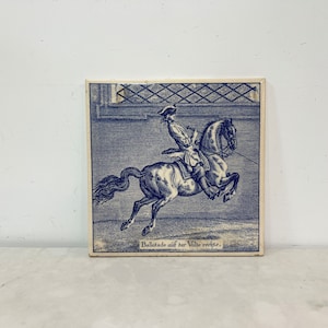 May include: Square ceramic tile with a blue and white illustration of a rider on a rearing horse. The rider is wearing a hat and coat. Text at the bottom reads "Ballotade auf der Völte rechts."