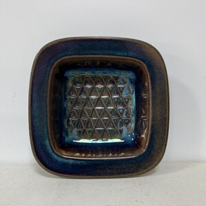 May include: A square ceramic dish with a blue and brown glaze. The dish has a geometric pattern on the inside.
