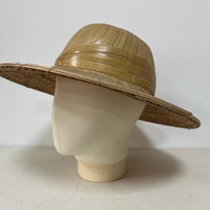 May include: A straw hat with a wide brim and a rounded crown. The hat is a light tan color and appears to be made of woven straw. The hat is displayed on a mannequin head.