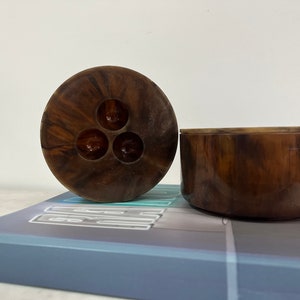 May include: Two wooden bowls, one with three circular cutouts, sitting on a book with the text "RA Now" on the cover.