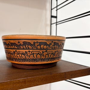 Puede incluir: Una taza de cerámica blanca con un asa negra y el texto "But First, Coffee" en negro y negrita. La taza está sobre una superficie blanca. La taza mide aproximadamente 10 cm de alto.