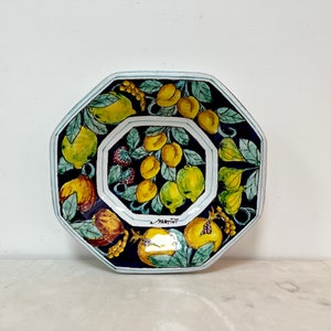May include: Octagonal ceramic plate with a blue background and a colorful design of lemons, pomegranates, and figs. The plate is signed "Martini" in the center.