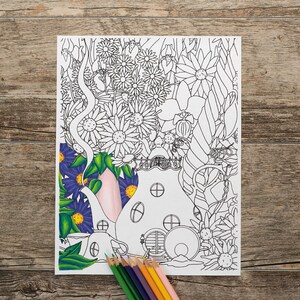 Op de afbeelding: Een zwart-witte kleurplaat met een theepotvormig huis met een deur en ramen. Het huis is omringd door bloemen en bladeren. Er liggen kleurpotloden op een houten oppervlak onder de pagina.