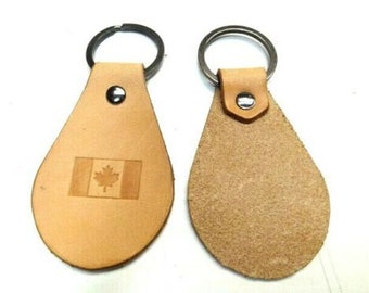 May include: Two leather keychains with metal rings. One keychain features a brown leather tag with a laser-engraved Canadian flag. The other keychain has a plain brown leather tag.