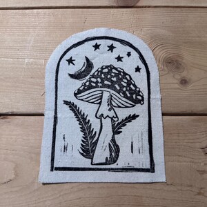May include: A black and white illustration of a mushroom with a crescent moon and stars in the background. The mushroom is printed on a white fabric patch.