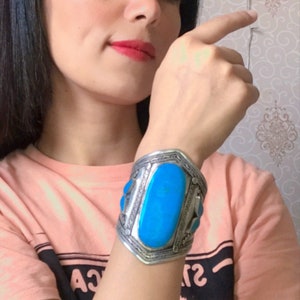 May include: A woman wearing a light pink t-shirt with black text and a silver bracelet with a large turquoise stone.