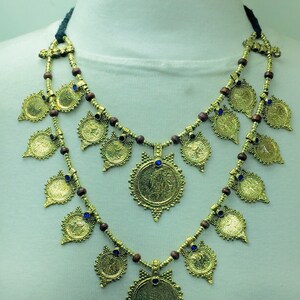 May include: A gold necklace with multiple round pendants and blue accents. The necklace is made of wood beads and metal.